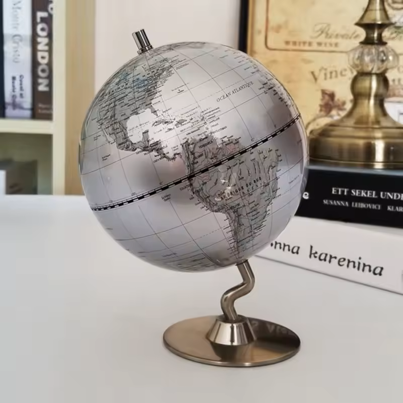 Globe terrestre décoratif design argent avec cartographie détaillée, monté sur un pied en métal, idéal pour décoration intérieure élégante.